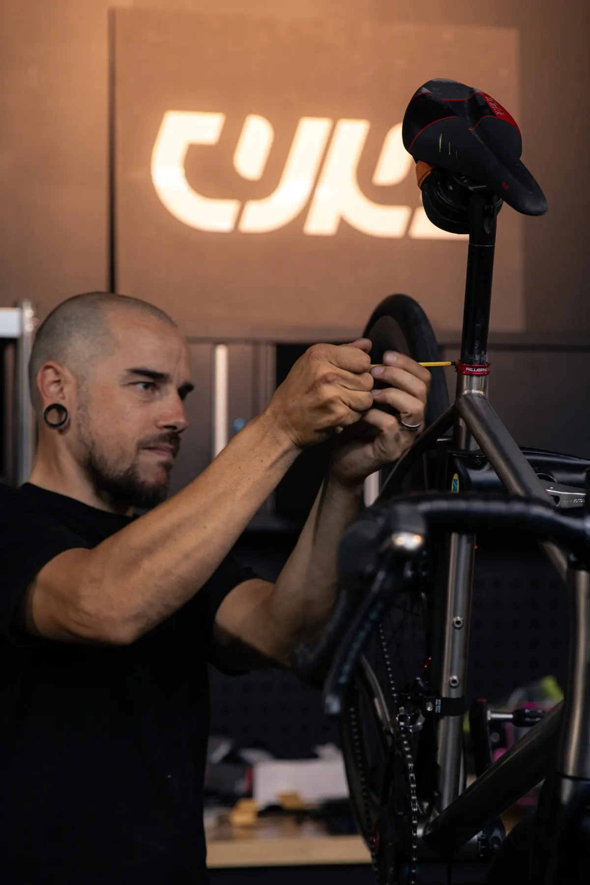 A mechanic adjusts the seat post of a titanium bike on the workshop stand, under the CYKL logo.
